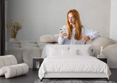 Young business woman using the phone and the computer sitting on the couch at home Wall mural